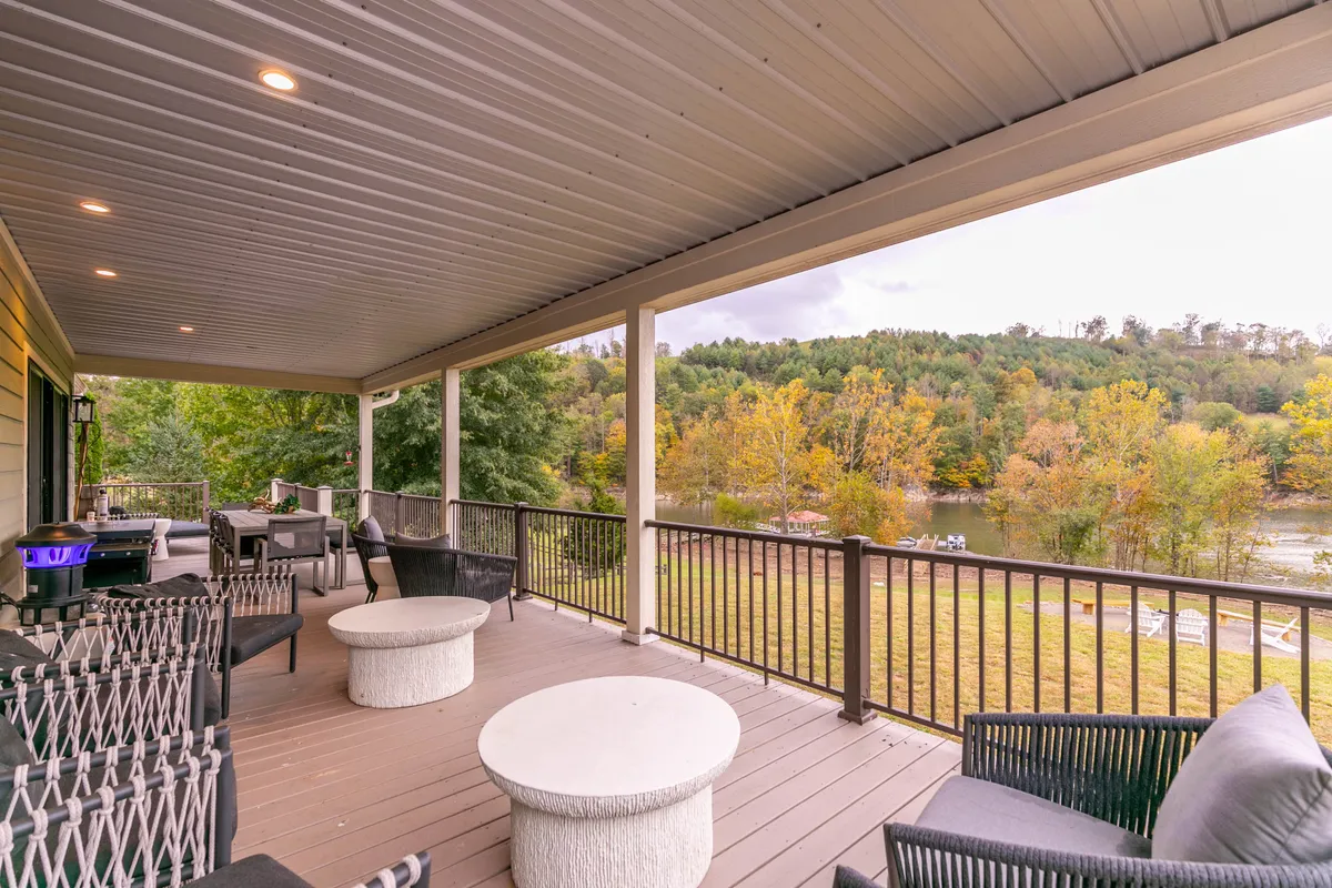 An inviting outdoor seating area overlooks a calm river, framed by trees and open sky. The atmosphere is peaceful and ideal for entertaining guests or unwinding in nature.