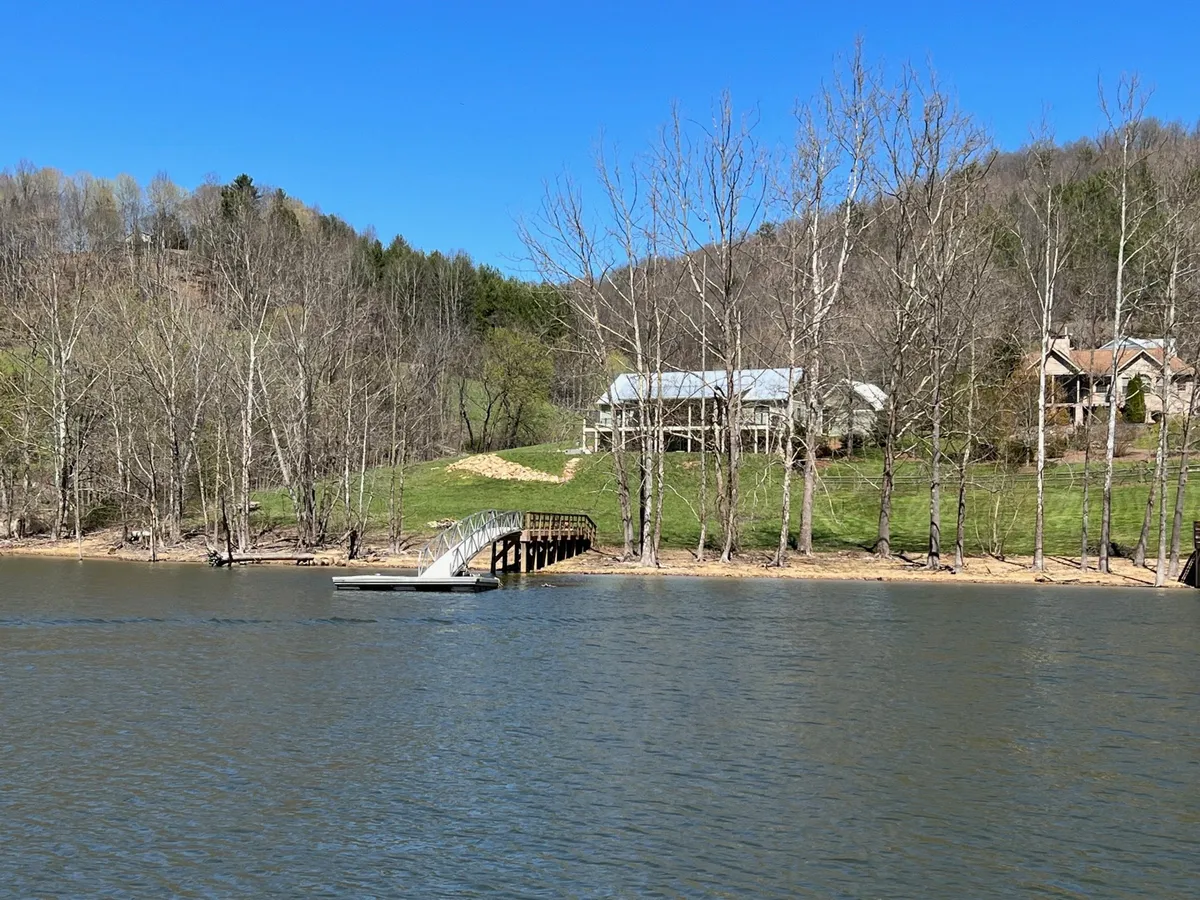 This image captures a serene dock extending into a calm lake, bordered by trees and featuring a house in the background. The waterside location conveys tranquility and the potential for lakeside activities.