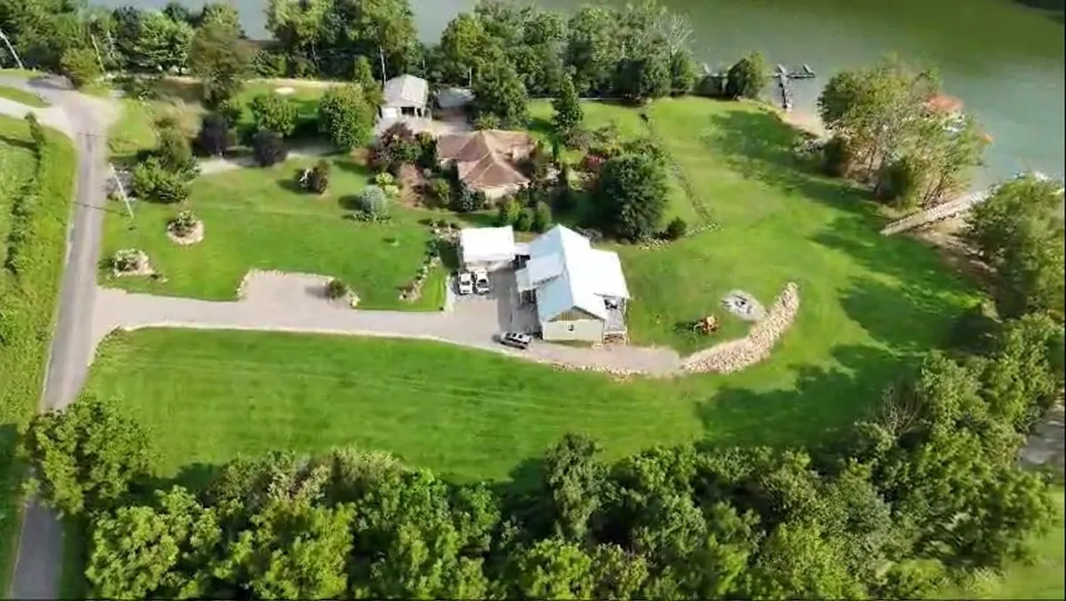 This image features an expansive green lawn surrounded by trees with glimpses of a nearby water body and various buildings. The landscape evokes a sense of tranquility and connection to the outdoors.
