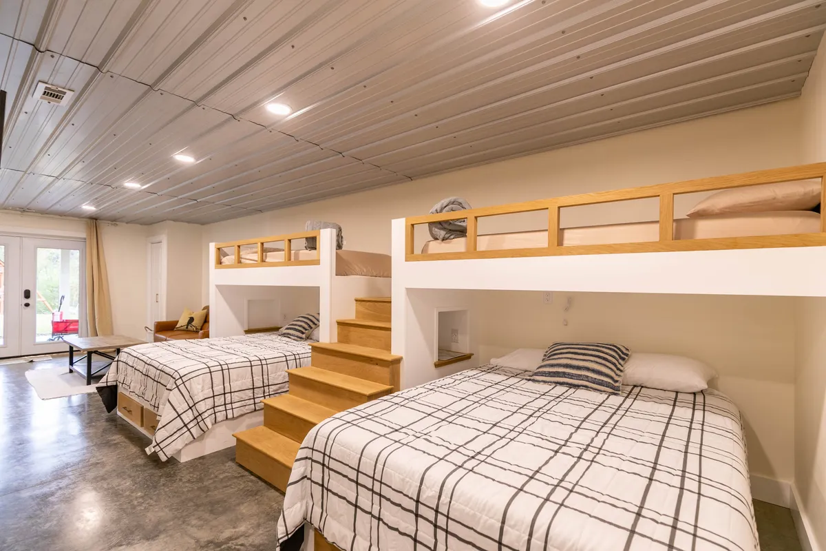 A playful and relaxed bunk suite features built-in bunk beds, a small staircase, and large windows that let in ample daylight. This space is designed for both comfort and fun, ideal for families or groups seeking a unique sleeping arrangement.