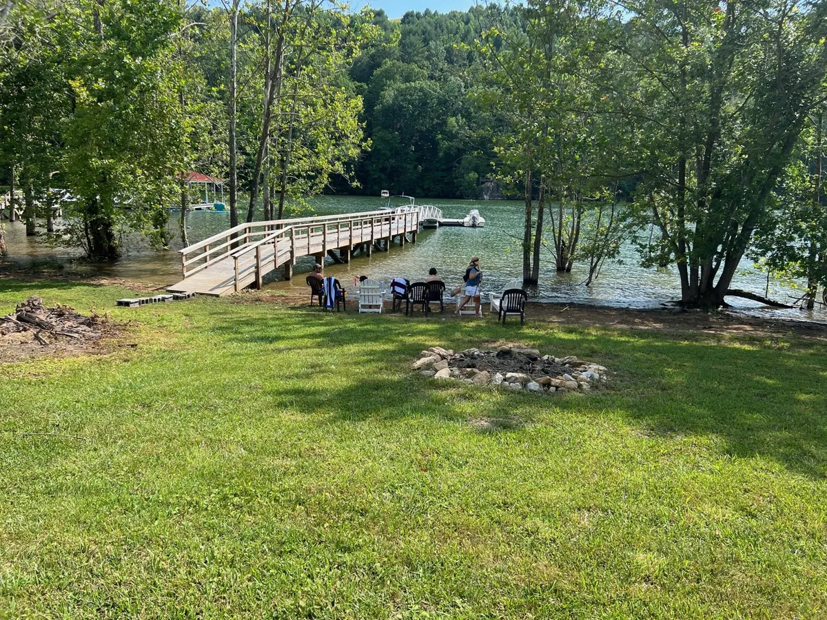 A serene setting by the waterfront, where a group sits around a fire pit on a wooden bridge. The scenic background features calm water and leafy surroundings, suggesting peaceful evenings and opportunities for group relaxation and connection.