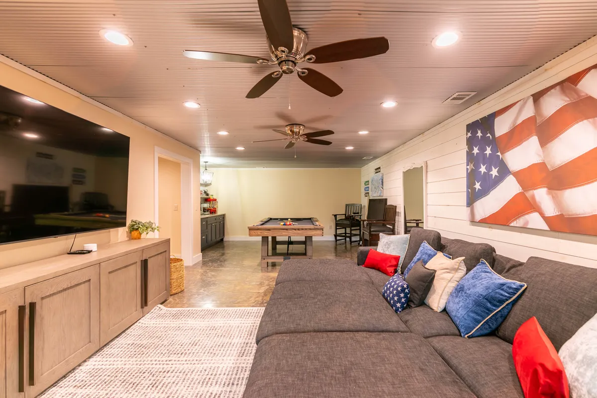 A spacious entertainment area with a large sectional sofa, pool table, wall-mounted television, and patriotic artwork. The layout naturally invites socializing, movie watching, and game nights.