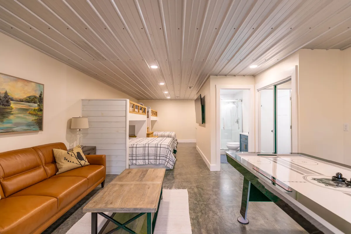 A playful and comfortable bunk suite featuring leather sofa seating, custom bunk beds, an air hockey table, and artwork on the wall. The space is designed for both relaxation and fun, perfect for group hangouts or family sleepovers. The various amenities in view—such as the bunk beds and air hockey table—emphasize the room’s versatility for both restful nights and lively game tournaments.