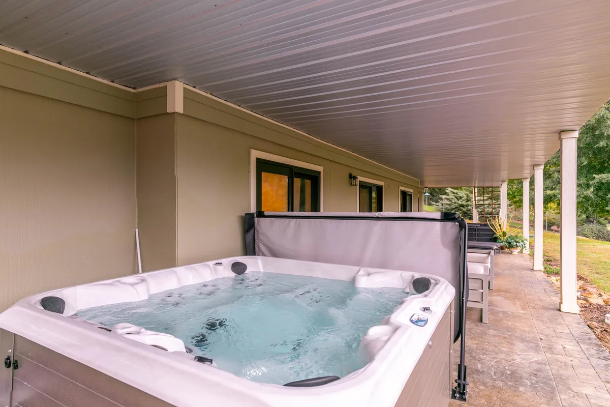 A relaxing patio area featuring a large 7-person hot tub nestled among greenery. The setting is peaceful and private, ideal for unwinding after a day of outdoor fun with resort-style amenities in view.