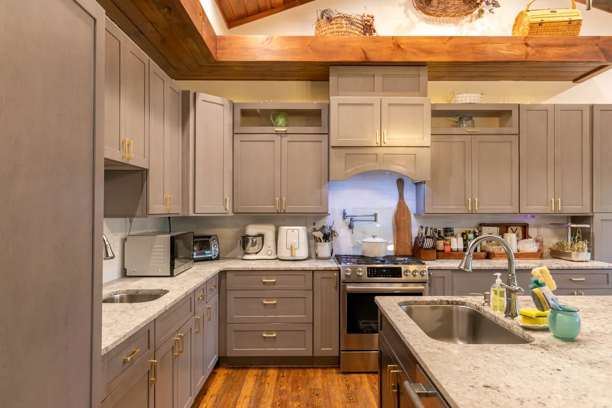 A warm, inviting kitchen featuring gleaming granite countertops, stainless steel appliances, wood accents, and gold hardware. The spacious island is central, perfect for meal prep and gathering, while open sight lines suggest an adjacent dining and living area.