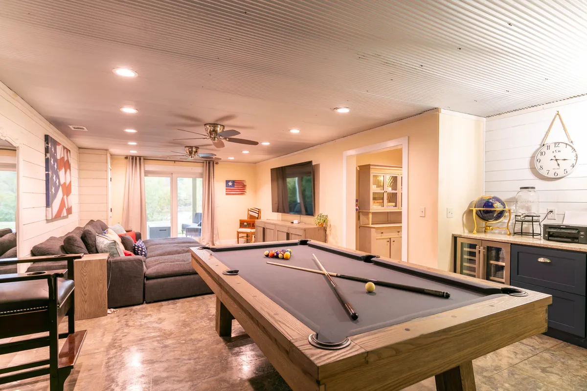 A modern game room featuring a pool table, comfortable sofa, wall-mounted TV, and stylish decorative elements. The space is designed for leisure and friendly competition, perfect for gatherings and game nights.