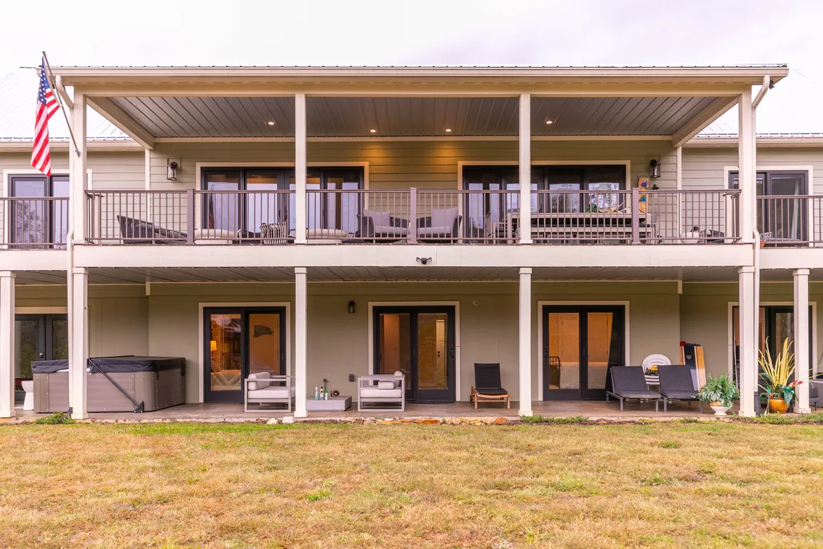 The image showcases a welcoming, two-story porch with ample outdoor seating, American flag, and large windows, all overlooking the surrounding landscape. The porch setting exudes relaxation and social gathering potential.