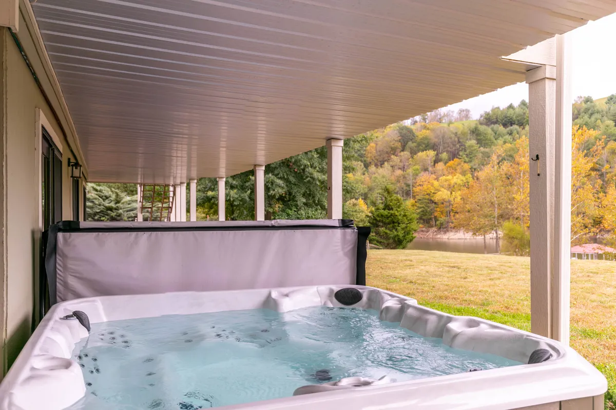 An inviting outdoor hot tub nestled beneath a patio cover, surrounded by lush nature. The setup offers a serene spot to relax, stargaze, or enjoy the sunset after a day of adventure.